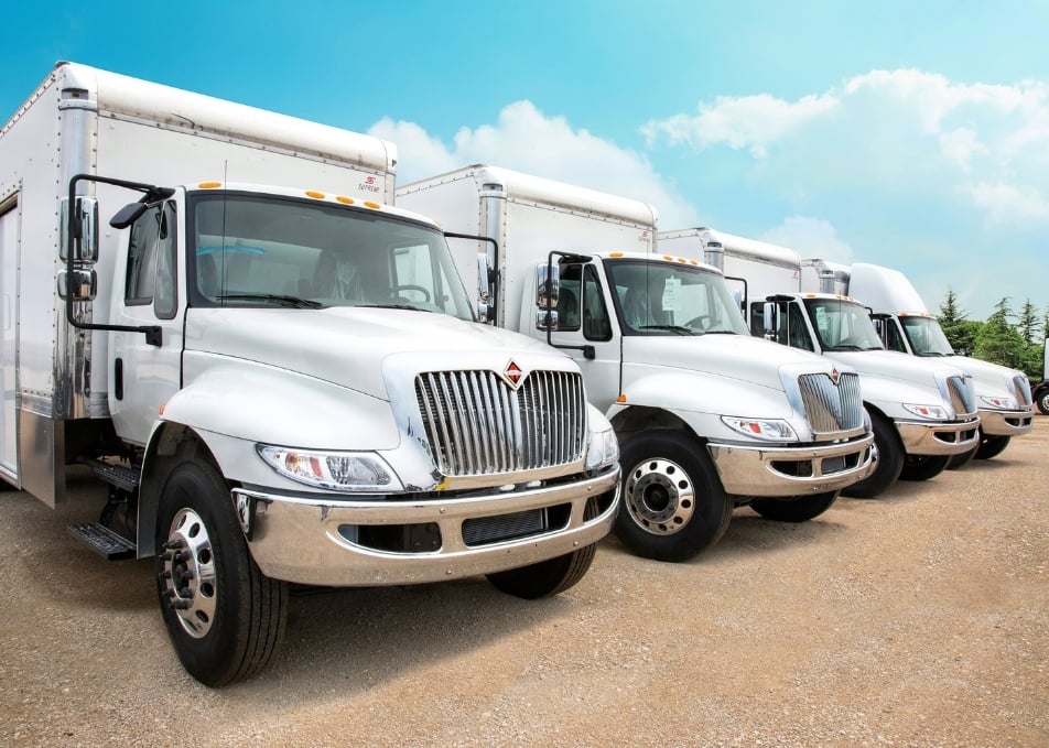 Lineup of four white fleet trucks with van bodies