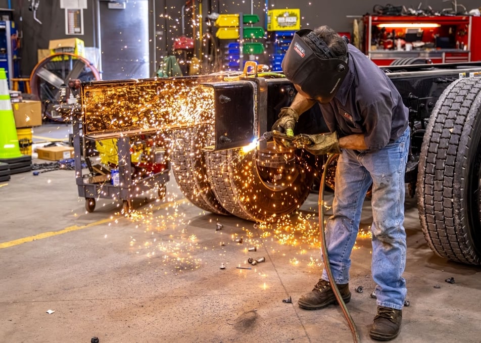 Technician welding two pieces of truck frame together