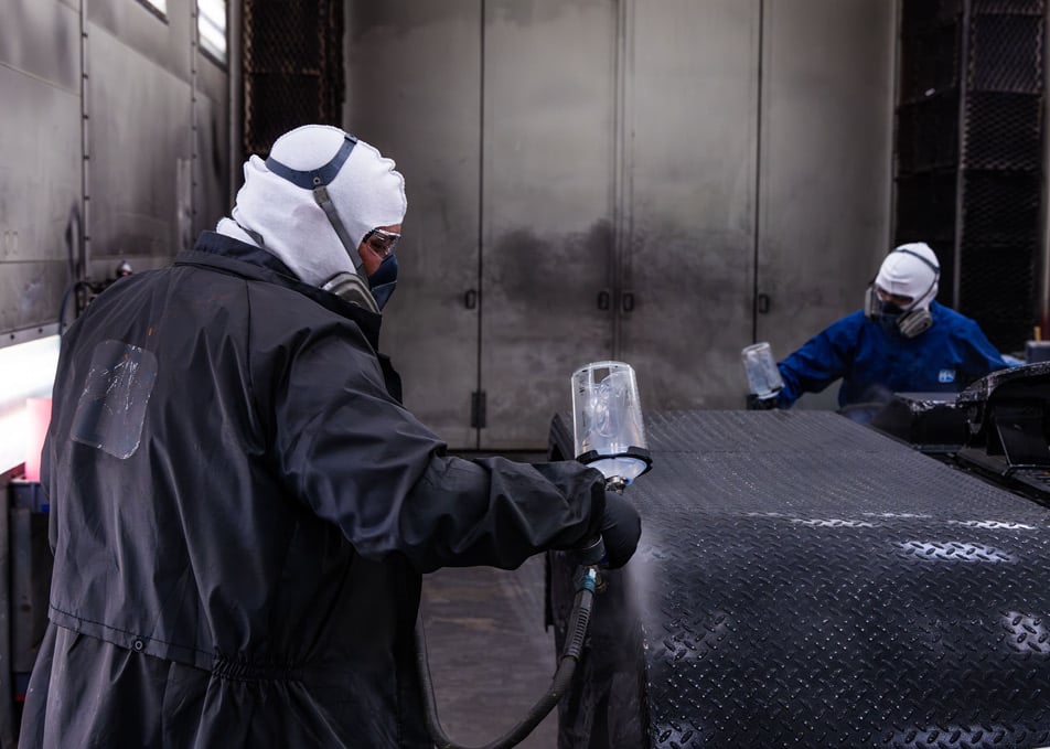 Two technicians using spray guns to paint custom truck fender black