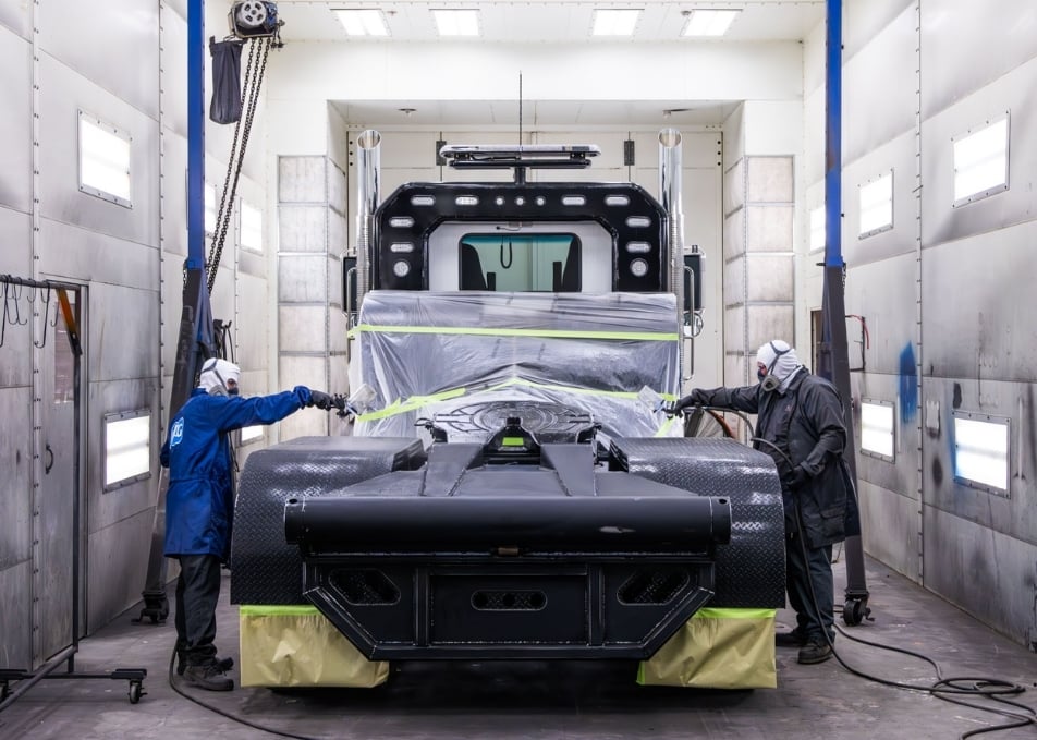 Zoomed out view of two technicans spray painting truck fenders black