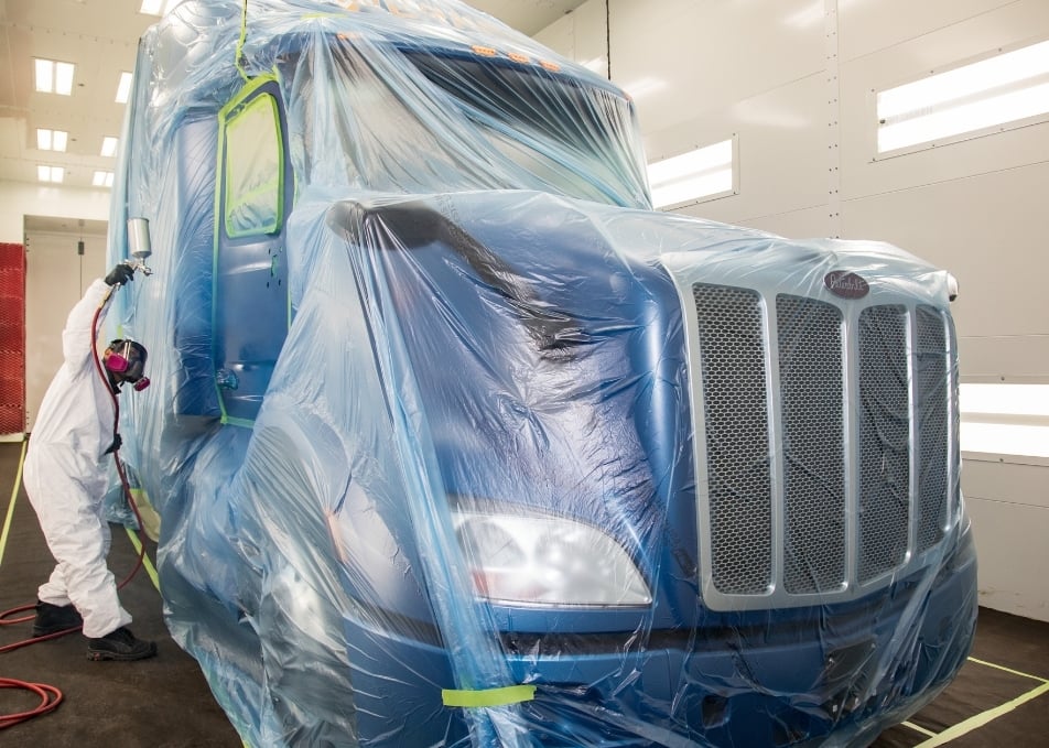 View of Peterbilt truck wrapped in plastic while the door is being painted blue