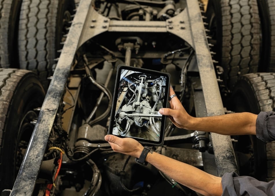 Technician taking photo of truck chassis cabling and hydraulics on tablet