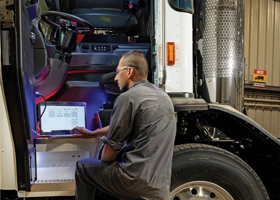 Technician working on laptop that's connected to truck electrical system