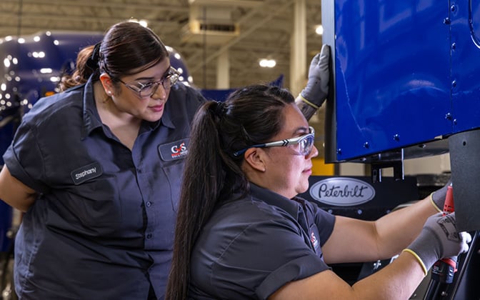 Two female technicians installing component on blue Peterbilt truck