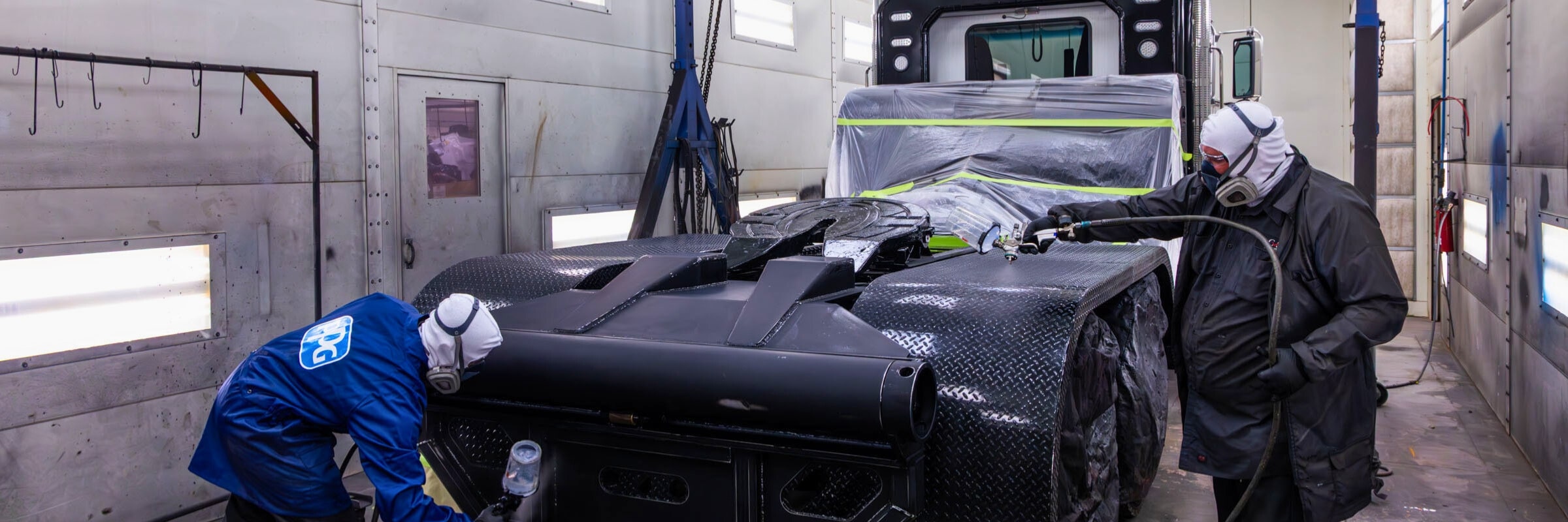 Two technicians spray painting custom truck fenders and winch with black paint